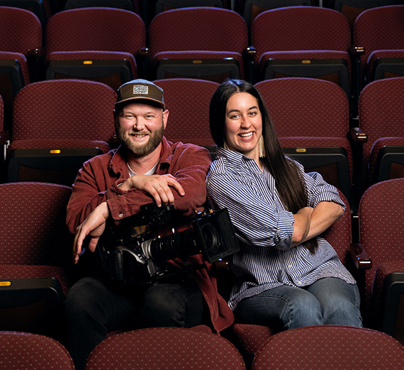 A woman in graduation cap and gown smiles at the camera